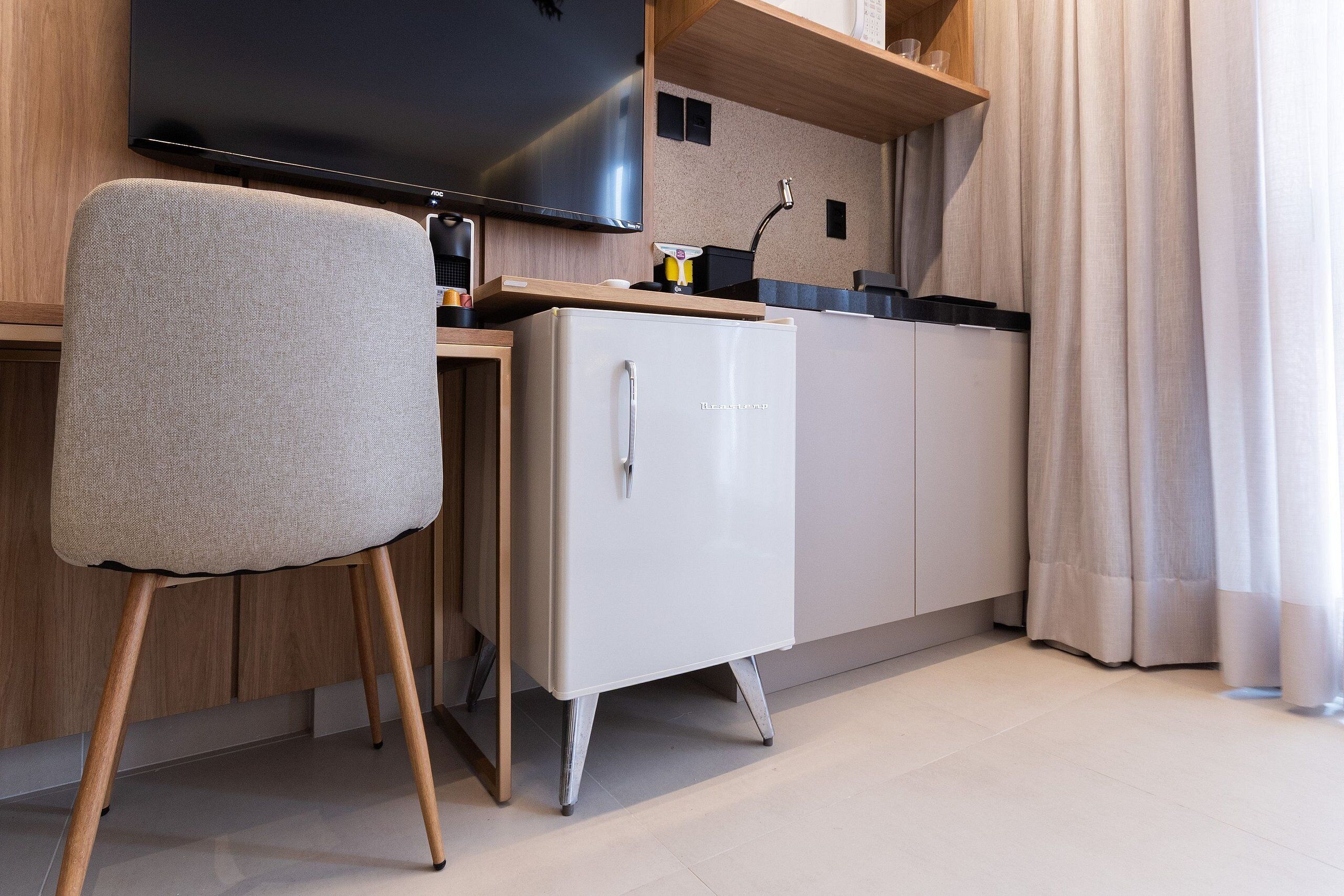 Une petite cuisine équipée avec un téléviseur à écran plat, un petit réfrigérateur et une chaise.