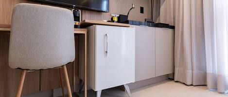Une petite cuisine équipée avec un téléviseur à écran plat, un petit réfrigérateur et une chaise.