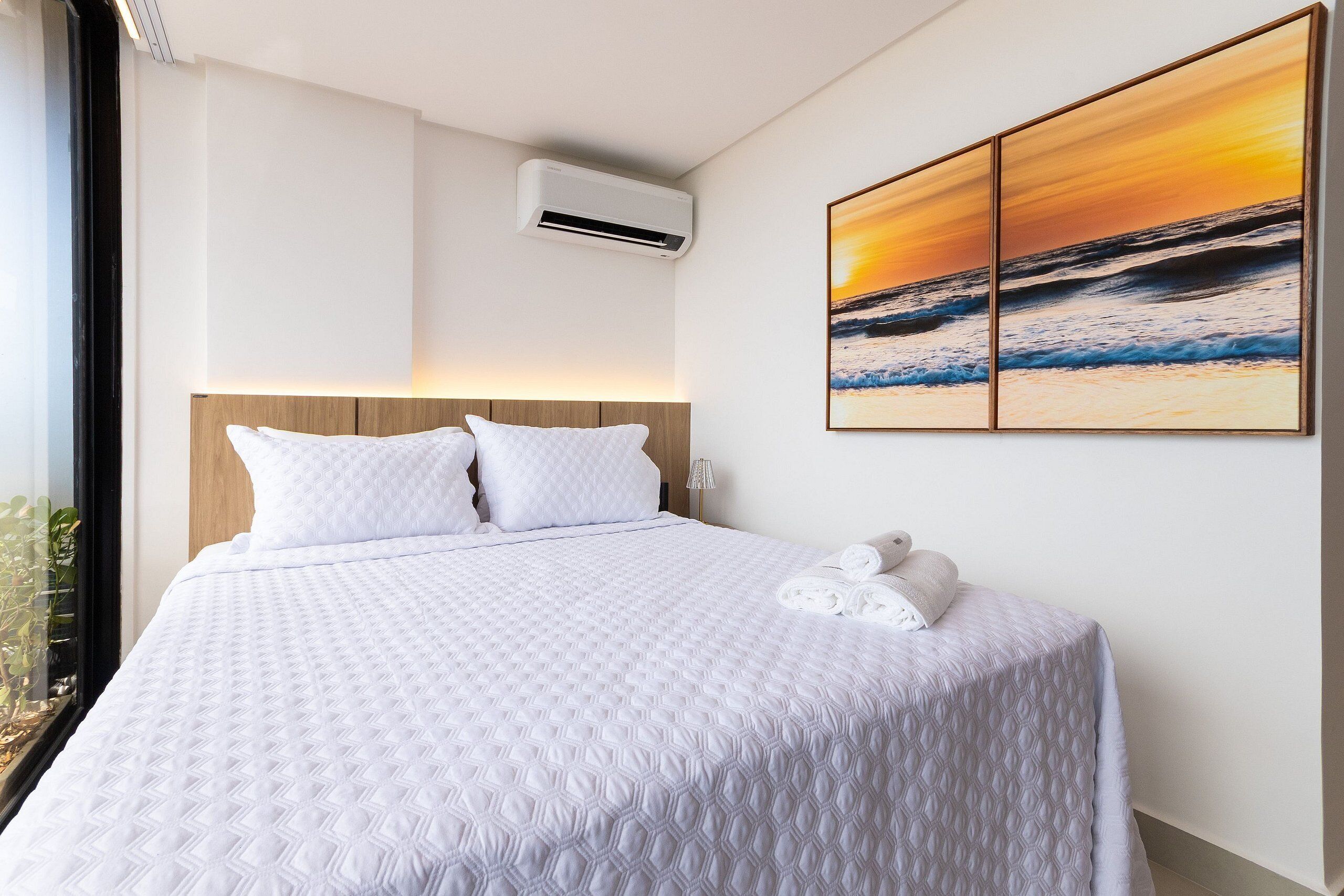 Habitación de hotel con una cama grande, un cabecero, un equipo de aire acondicionado y una pintura de atardecer en la pared.