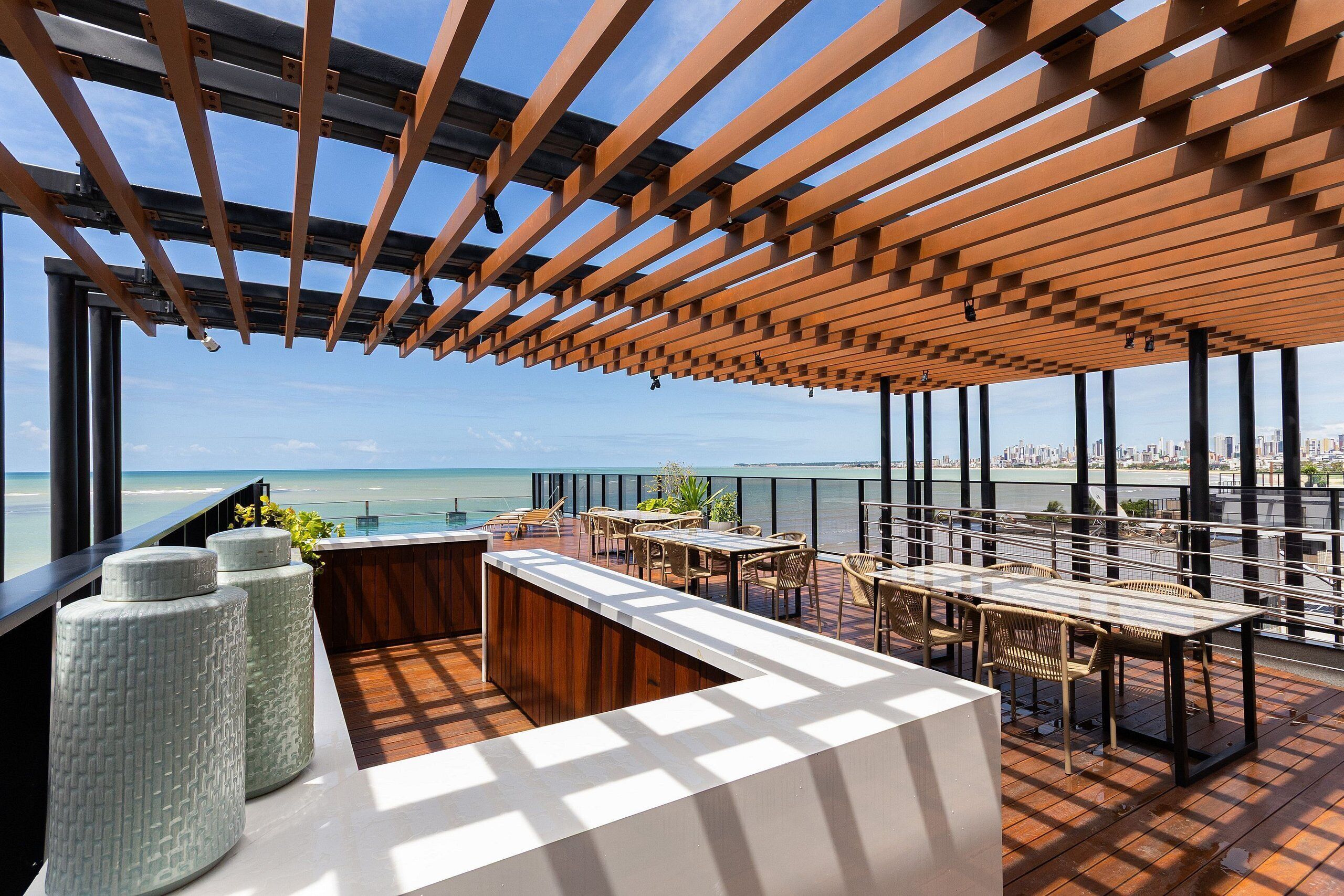 Une terrasse sur le toit dotée d’une pergola en bois, d’un espace salon extérieur et offrant une vue sur l’océan.