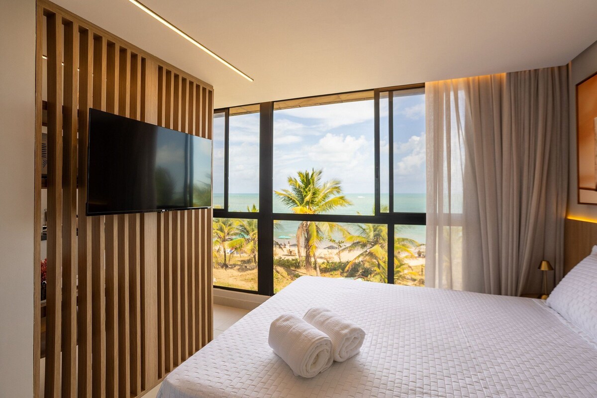 A hotel room with a large window offering a view of the beach and palm trees.