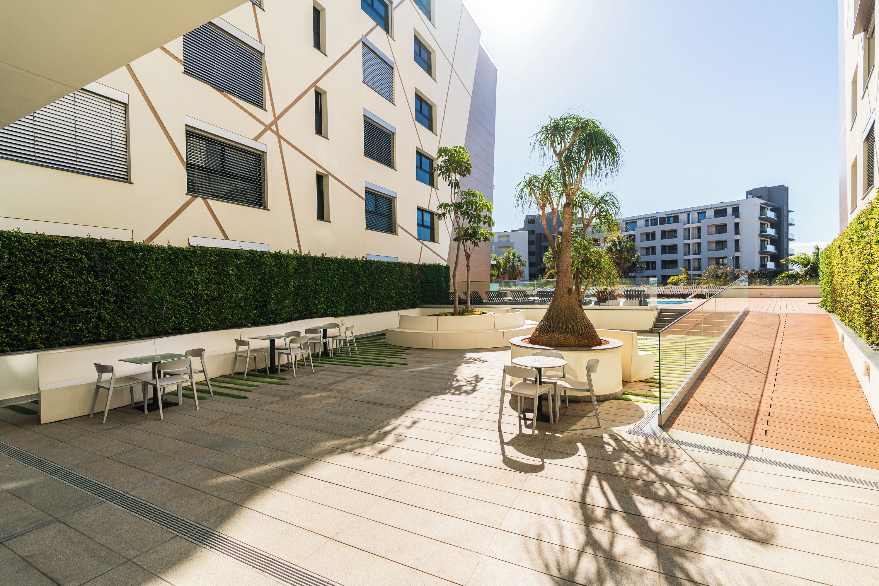 Un espace extérieur aménagé en terrasse, avec des sièges, un arbre au centre et un bâtiment moderne en arrière-plan.
