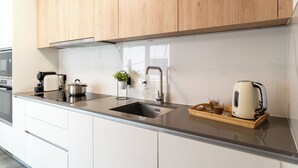 Una cucina moderna con mobili in legno, un lavello in acciaio inossidabile, un bollitore, una macchina per il caffè e un vassoio con un bicchiere e una tazza.