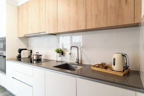 A modern kitchen with wooden cabinets, a stainless steel sink, a kettle, a coffee maker, and a tray with a glass and a cup. - Four Seasons in Funchal... where luxury meets tranquility! (Funchal)