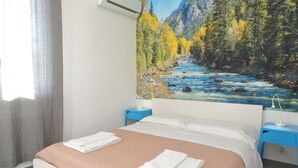 Een hotelkamer met een bed, twee nachtkastjes, een schilderij van een rivier en een raam met gordijnen.