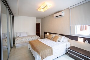 A bedroom with a bed, bedside table, and an air conditioning unit. - Garden House - Bessa Beach by Carpediem (João Pessoa)