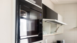 Eine Küche mit integriertem Mikrowellenherd und Backofen, weißen Schränken und einer Edelstahl-Spritzschutzwand.