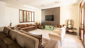 Ein modernes Wohnzimmer mit großem Fernseher, einem Glastisch und einer Sofagarnitur.