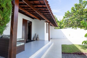 A covered outdoor area with a wooden pergola, a wicker sofa with cushions, and a pair of stone vases.