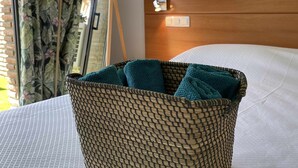 Una cesta de mimbre con toallas color turquesa sobre una cama con sábanas blancas.