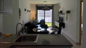 Una cocina moderna con una isla central, un comedor con mesa de vidrio y vistas a un edificio.