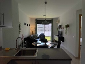 A modern kitchen with a central island, a dining area with a glass table, and a view of a building outside. - Renovated apartment near the beach (Lloret De Mar)