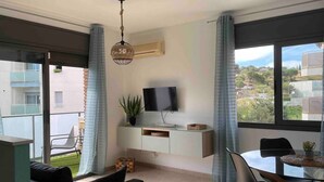 Un salon moderne doté d’un téléviseur à écran plat, d’une table à manger et d’un balcon offrant une vue sur la ville.