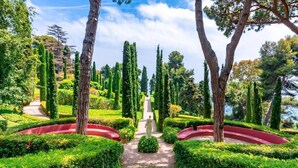 Un jardin à la française, avec une statue centrale, des haies soigneusement taillées et de grands arbres.
