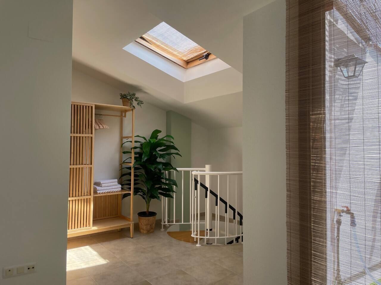 Una habitación con tragaluz, un armario de madera, una planta en maceta y una escalera.