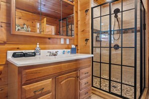 A wooden cabin bathroom with a vanity, mirror, and shower enclosure. - 10 Min from Dollywood! 2 Fireplaces •Private Hot tub• Amazing Mtn Views! (Sevierville)