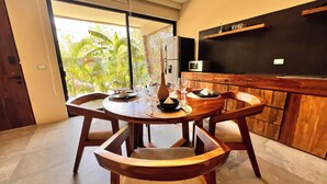 A dining area with a round wooden table, chairs, and a view of greenery outside. - Private and Peaceful Apartment 1BD 1BR (Tulum)