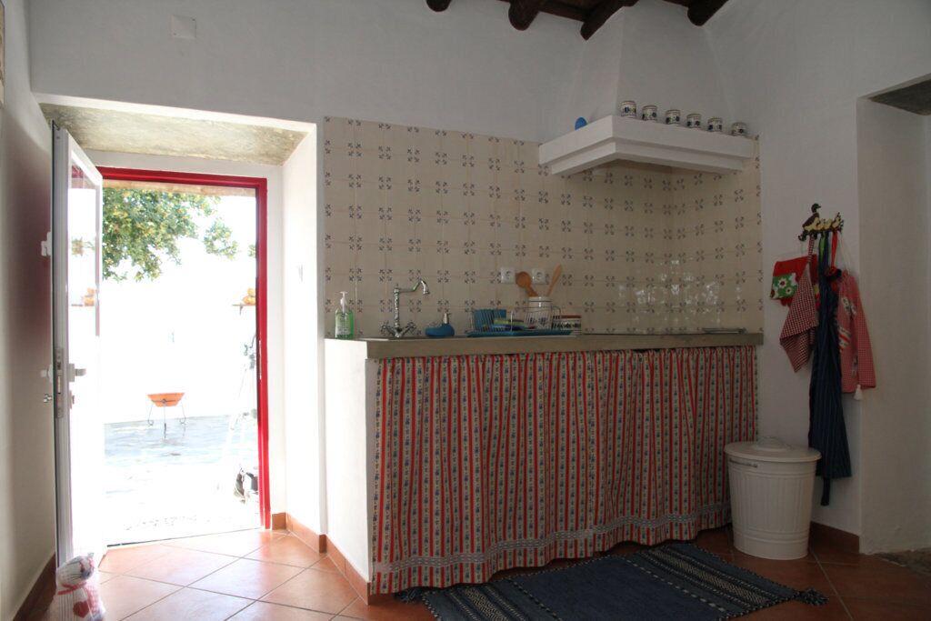 Een keuken met betegelde vloer, een gestreept gordijn, een spoelbak en een raam met uitzicht op een terras.