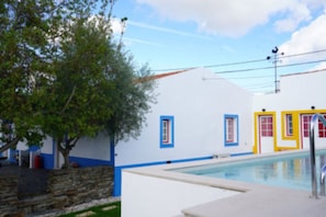 A pool area with a white building, blue and yellow doors, and a stone wall.