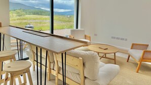 Una habitación moderna con un ventanal grande, una mesa de madera, un sofá y una silla.