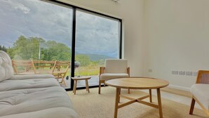 Una habitación amplia con un gran ventanal corredero que da a una terraza exterior, una mesa redonda de madera y un sofá.