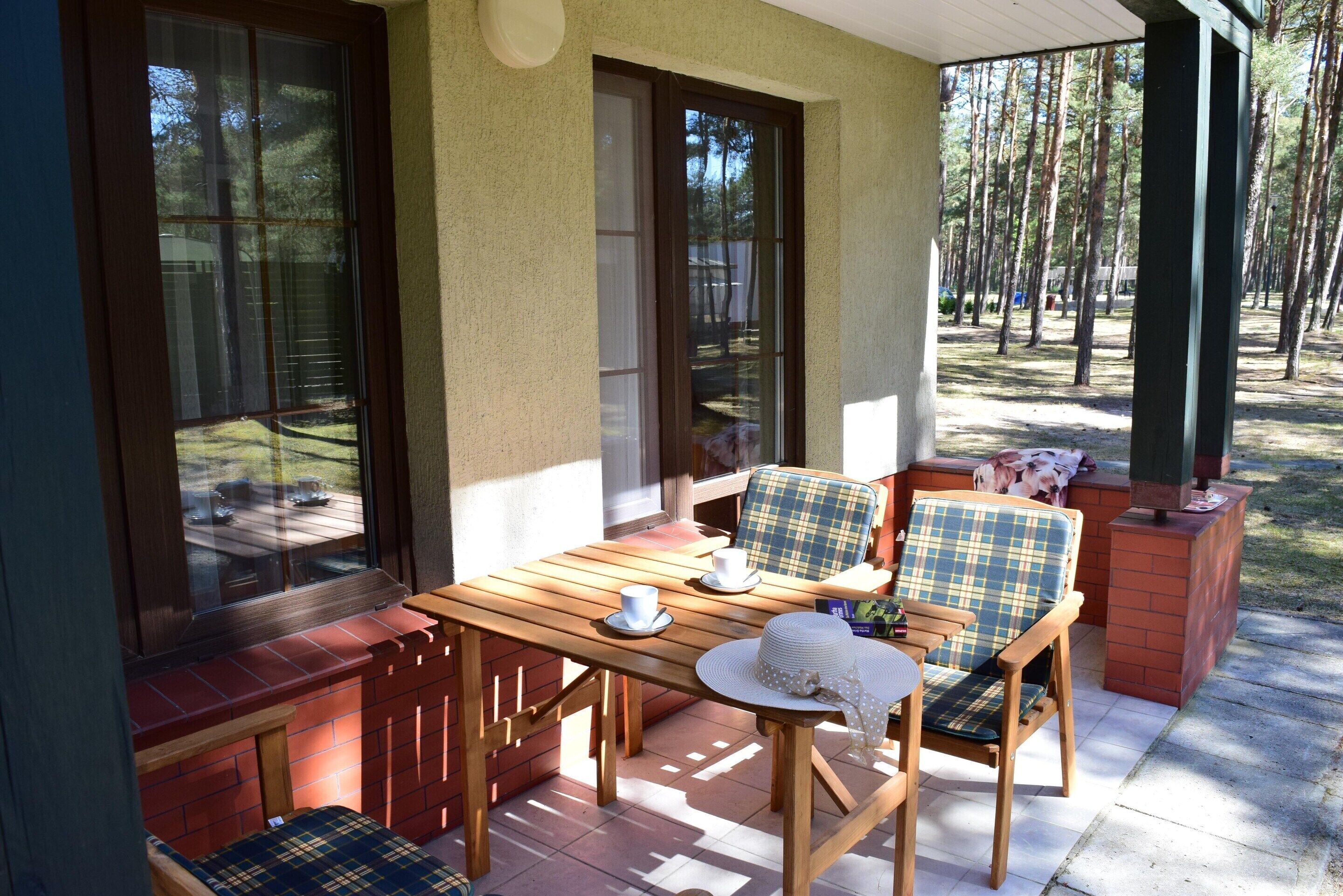 A covered patio with a wooden table and two plaid chairs, a white hat, and a cup on the table.