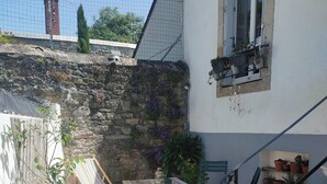 Une terrasse avec une table en bois et des chaises à rayures, un pot de fleurs et un mur de pierre orné de plantes grimpantes.