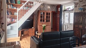 Un salon avec un canapé en cuir noir, des étagères en bois, un meuble en bois, un escalier et un téléviseur.