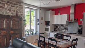 Une cuisine moderne avec des meubles blancs, un mur d’accent rouge et un coin repas comprenant une table et des chaises en bois.