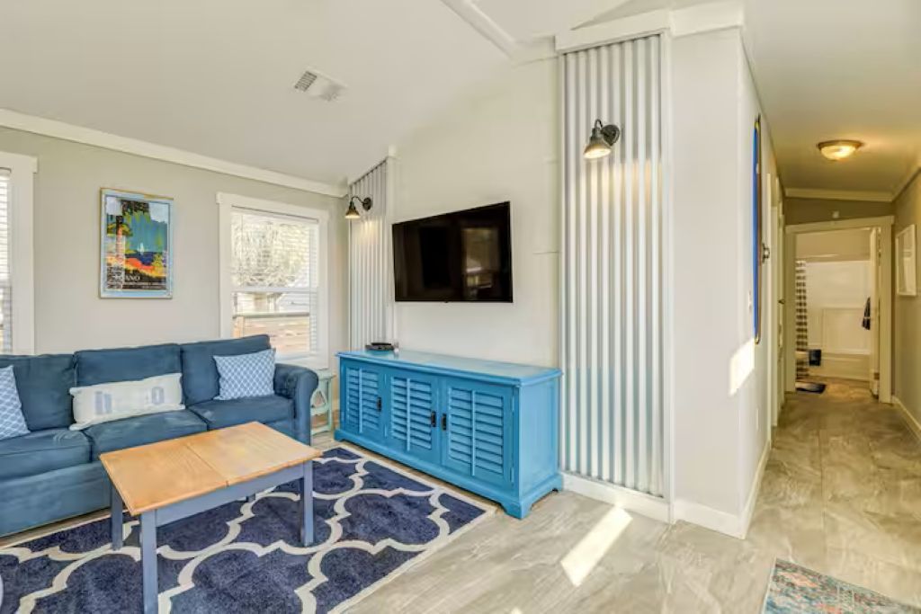 Una sala de estar con un sofá azul, una mesa de centro, un mueble azul, un televisor de pantalla plana y una alfombra estampada.