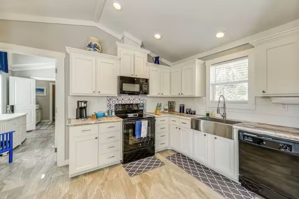 Una cucina moderna con mobili bianchi, piano cottura nero e lavandino in acciaio inossidabile.