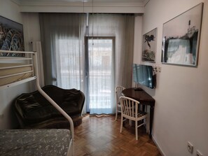 Ein Zimmer mit einem Bett, einem Schreibtisch, einem Sessel, einem Fernseher und einem fenster mit Vorhängen.