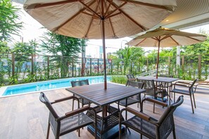 A poolside area with wooden tables and chairs, umbrellas, and a view of the pool and greenery. - Parque Shopping #706 - Apt in Pina by Carpediem (Recife)