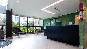 Un área de recepción con un mostrador oscuro, un extintor y una ventana con vistas a la vegetación.