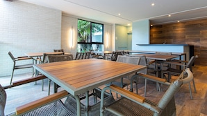 Un comedor moderno con mesas de madera y sillas de mimbre, paredes de ladrillo blanco y un ventanal con vistas a la vegetación.