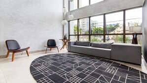 Una sala de estar moderna con un ventanal grande, un sofá gris, dos sillas negras y una alfombra de diseño en blanco y negro.