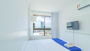 Una habitación de hotel con una cama, un televisor, una ventana con vistas a la ciudad y un aire acondicionado.