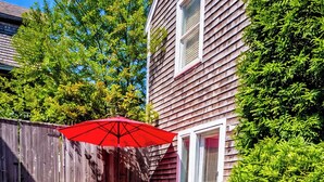 A wooden deck with a red umbrella, a small table, and a chair.