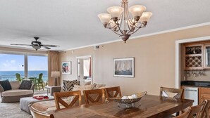A spacious dining area with a wooden table and chairs, a chandelier, and a view of the ocean.