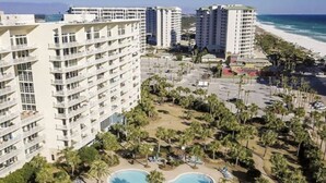 A resort with multiple high-rise buildings, a central swimming pool with palm trees, and a beach in the background.