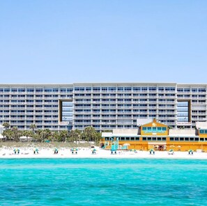A large hotel with multiple floors and balconies, situated by a beach with clear turquoise water. - Good Times foreshore water view condo (Destin)