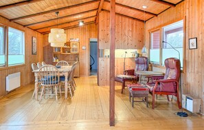 Interior acolhedor de uma cabana com mesa de jantar de madeira, cadeiras, um sofá e uma pequena cozinha.