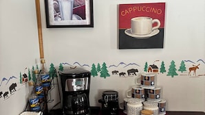 Uma estação de café com uma cafeteira, garrafas de xarope Torani e uma pilha de canecas de café sobre uma mesa.