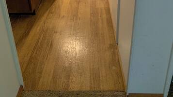A hallway with wooden flooring, a kitchen area on the left, and a door on the right.