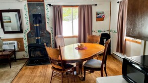 Uma sala de estar acolhedora com uma mesa de jantar de madeira, cadeiras, lareira, televisão e janela com cortinas.