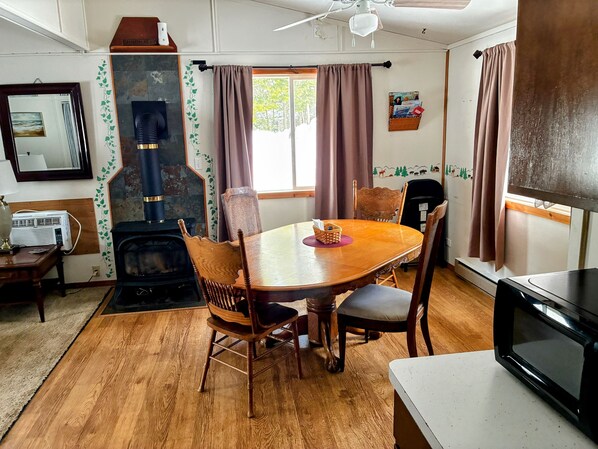 A cozy living room with a wooden dining table, chairs, a fireplace, a television, and a window with curtains.