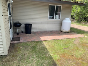 A house with a brick pathway leading to the front door, a window, a black grill, and a white water tank.