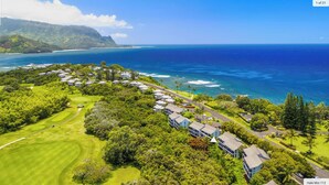 An aerial view of a coastal resort with a golf course, beachfront properties, and lush greenery. - Hideaways Retreat Villa- North shore princeville (Princeville)
