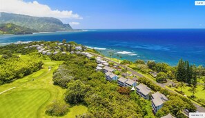 An aerial view of a coastal resort with a golf course, beachfront properties, and lush greenery.