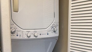 A compact washer and dryer unit with a control panel, located in a small laundry room with a wooden floor. - Hideaways Retreat Villa- North shore princeville (Princeville)